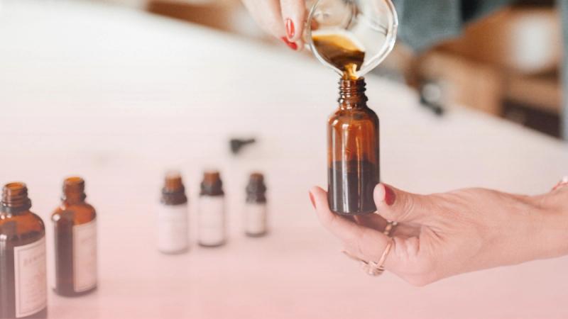 Manos preparando un remedio natural en gotas desde un frasco ámbar, representando los tratamientos de nuestro médico homeópata y flores de bach.