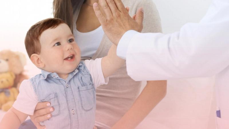 Médico chocando los cinco alegremente con un niño pequeño sostenido por su madre, reflejando la confianza de nuestro consultorio de puericultura.