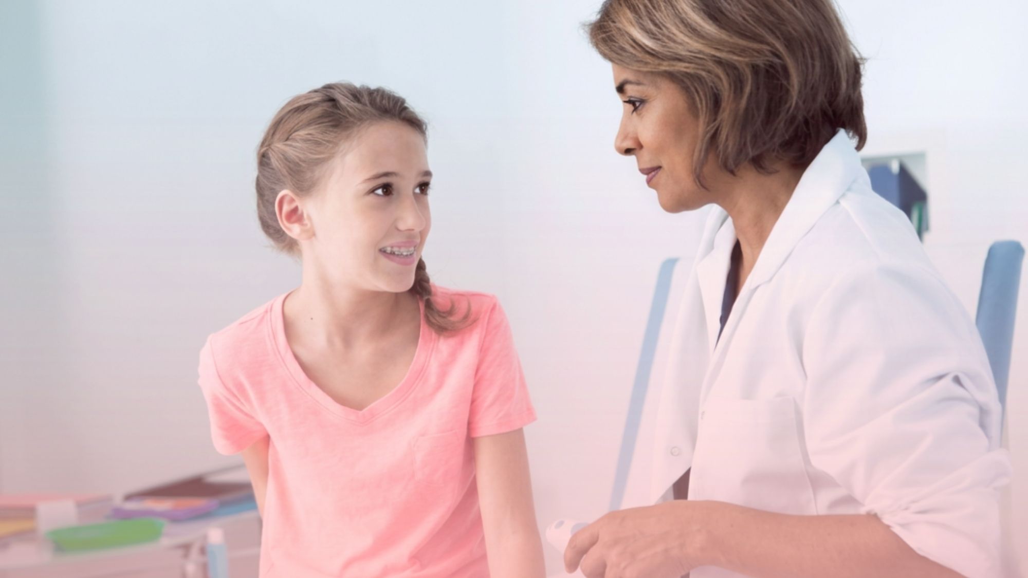 Médica conversando amigablemente con una niña y su madre en el consultorio, brindando un entorno de confianza en la primera consulta ginecológica