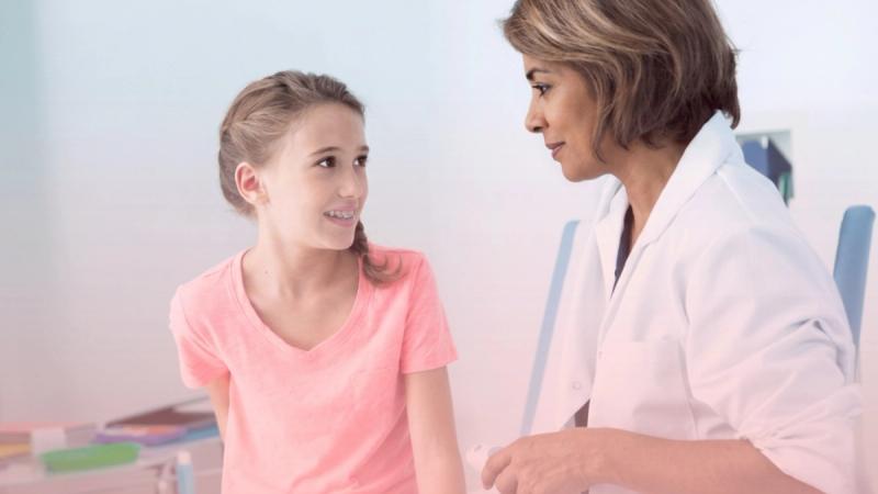 Médica conversando amigablemente con una niña y su madre en el consultorio, brindando un entorno de confianza en la primera consulta ginecológica