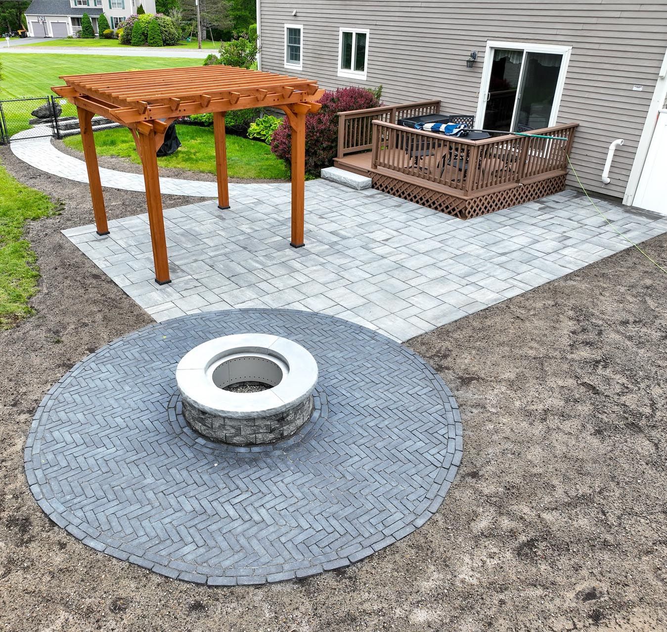 Completed residential hardscaping project featuring a paver patio, fire pit, pergola, and composite deck by Contrast Landscape
