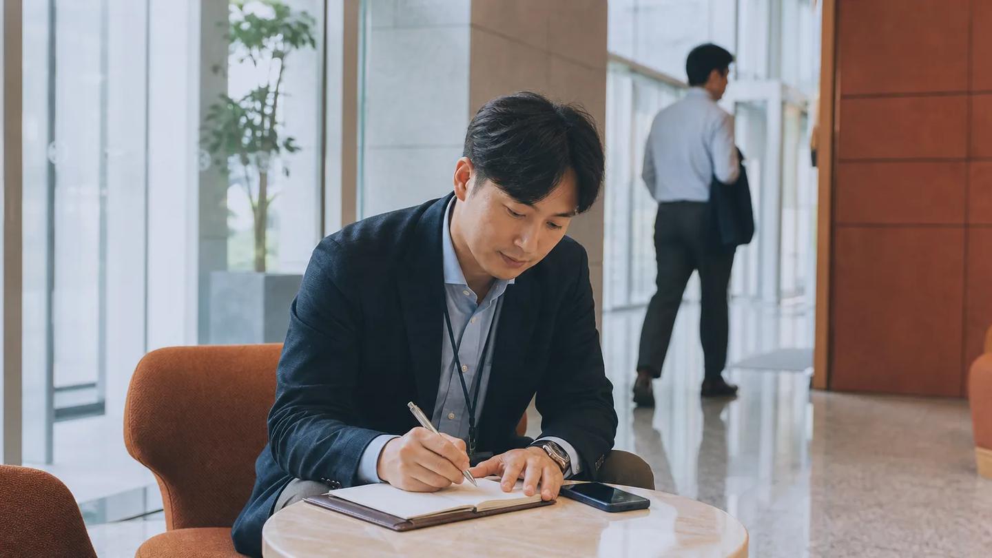 거래처 현장에서 고객과 대화한 뒤 노트에 방문 내용을 정리하는 영업 담당자