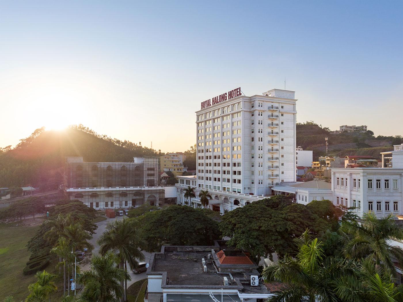 An aerial view of the hotel complex at sunrise, the sun rising behind a green hill with palms and treetops in the foreground