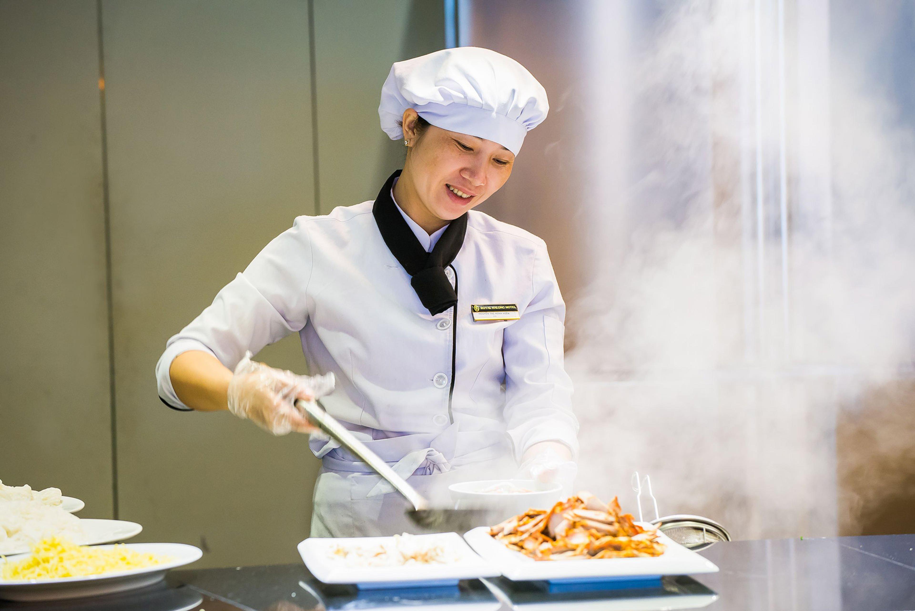 A chef in a white toque lifting fried food onto a plate with tongs, steam rising around his hands
