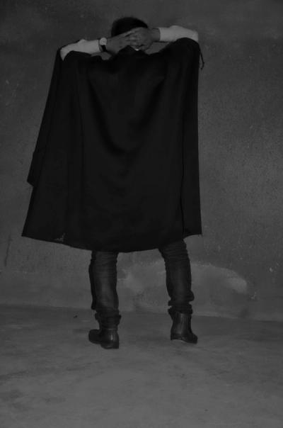Sexy queer man in a black poncho. Avant garde fashion. Haute de couture. Tribal postapocaliptic fashion.