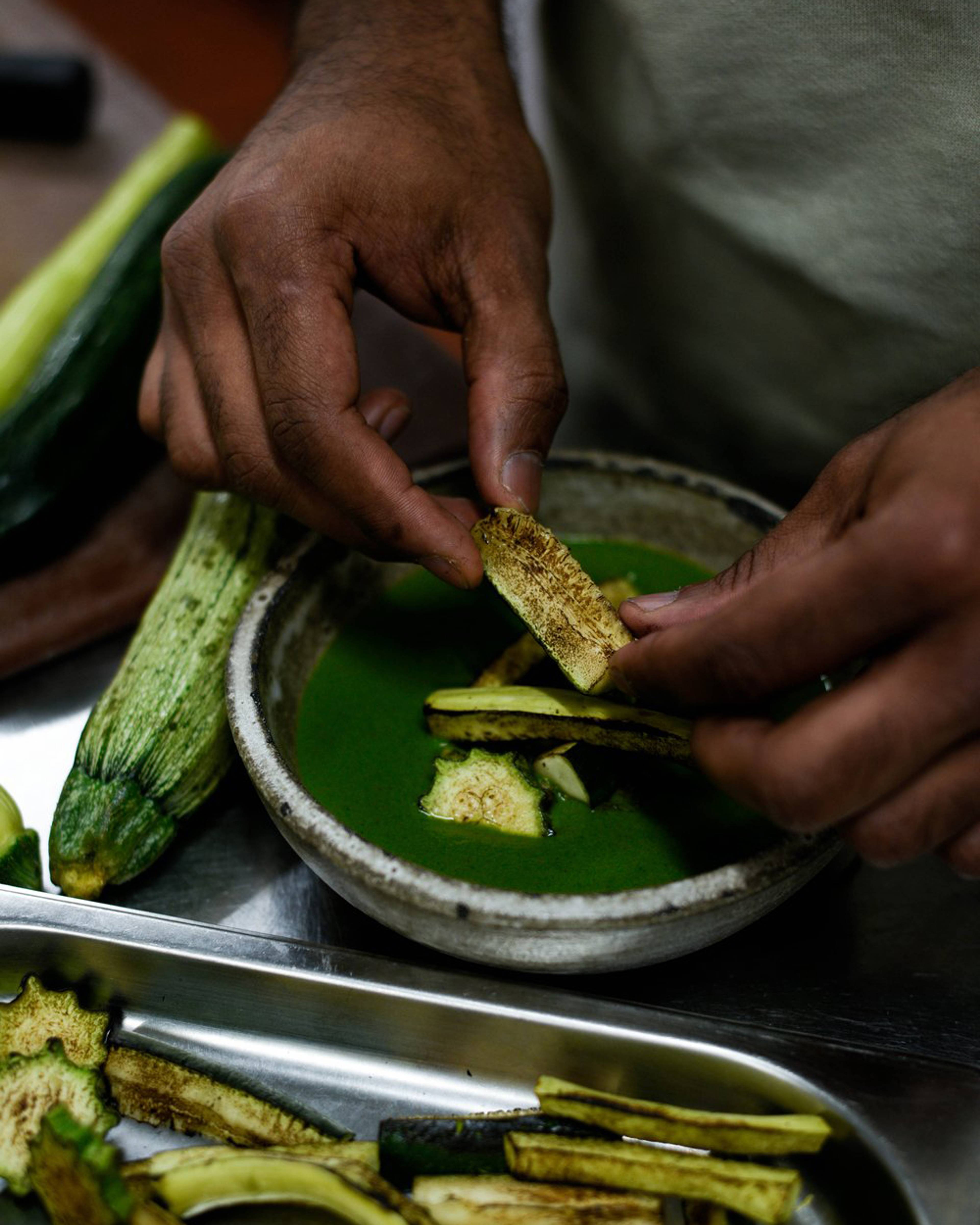 Sliced courgette being placed in the sauce