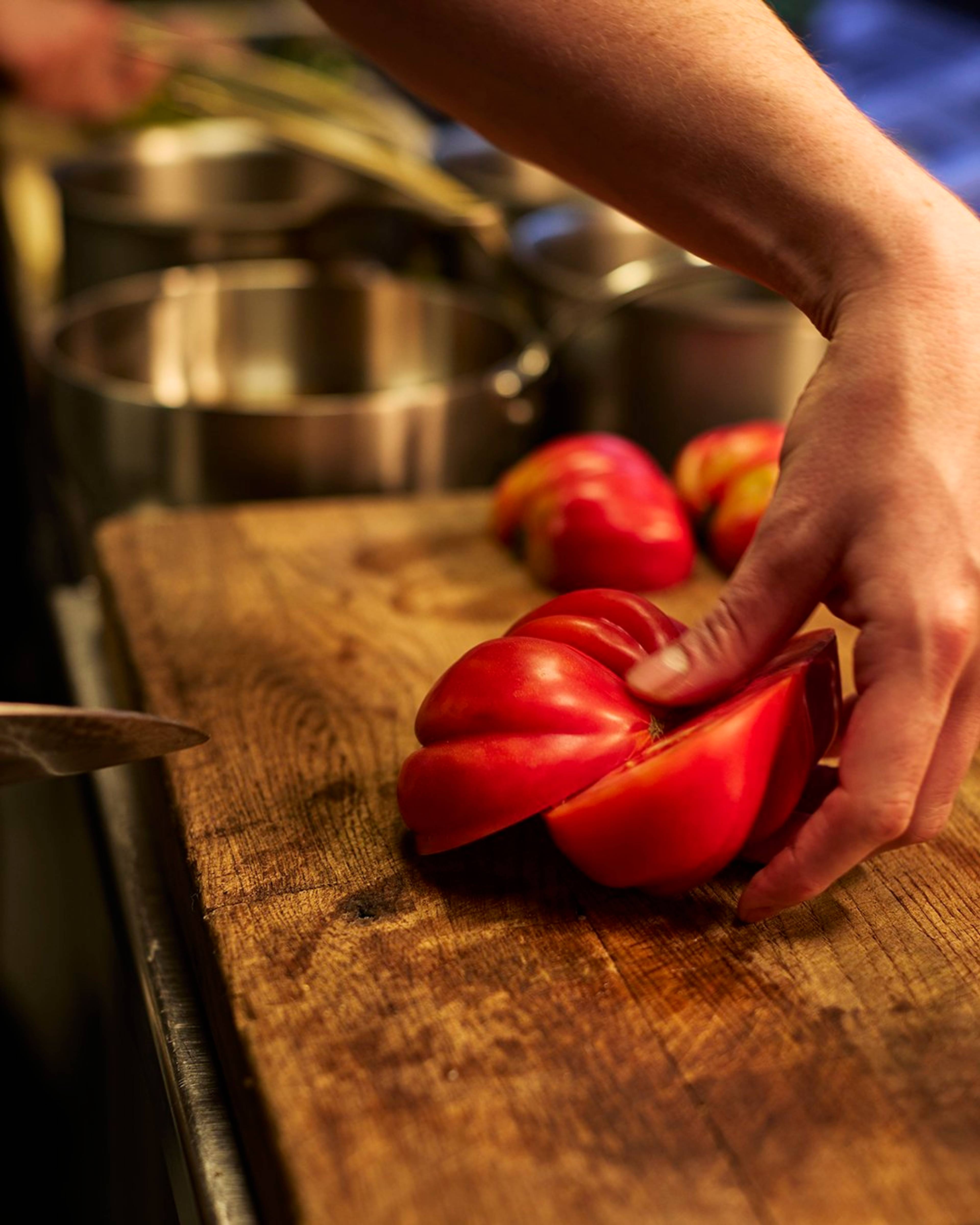 tomato being sliced in half on a wooden chopping board