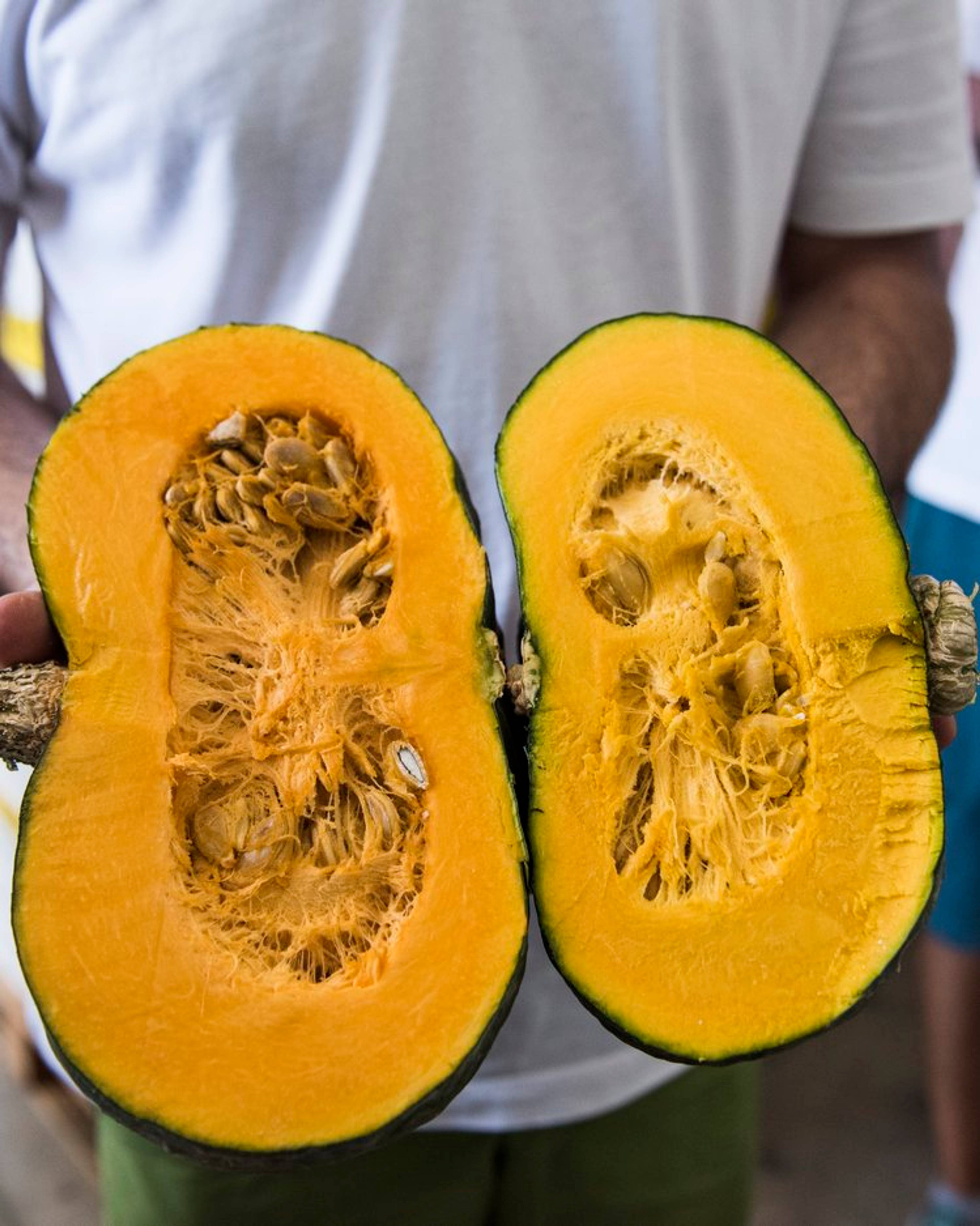 man holding delica pumpkin cut in half so you can see the colour and the seeds