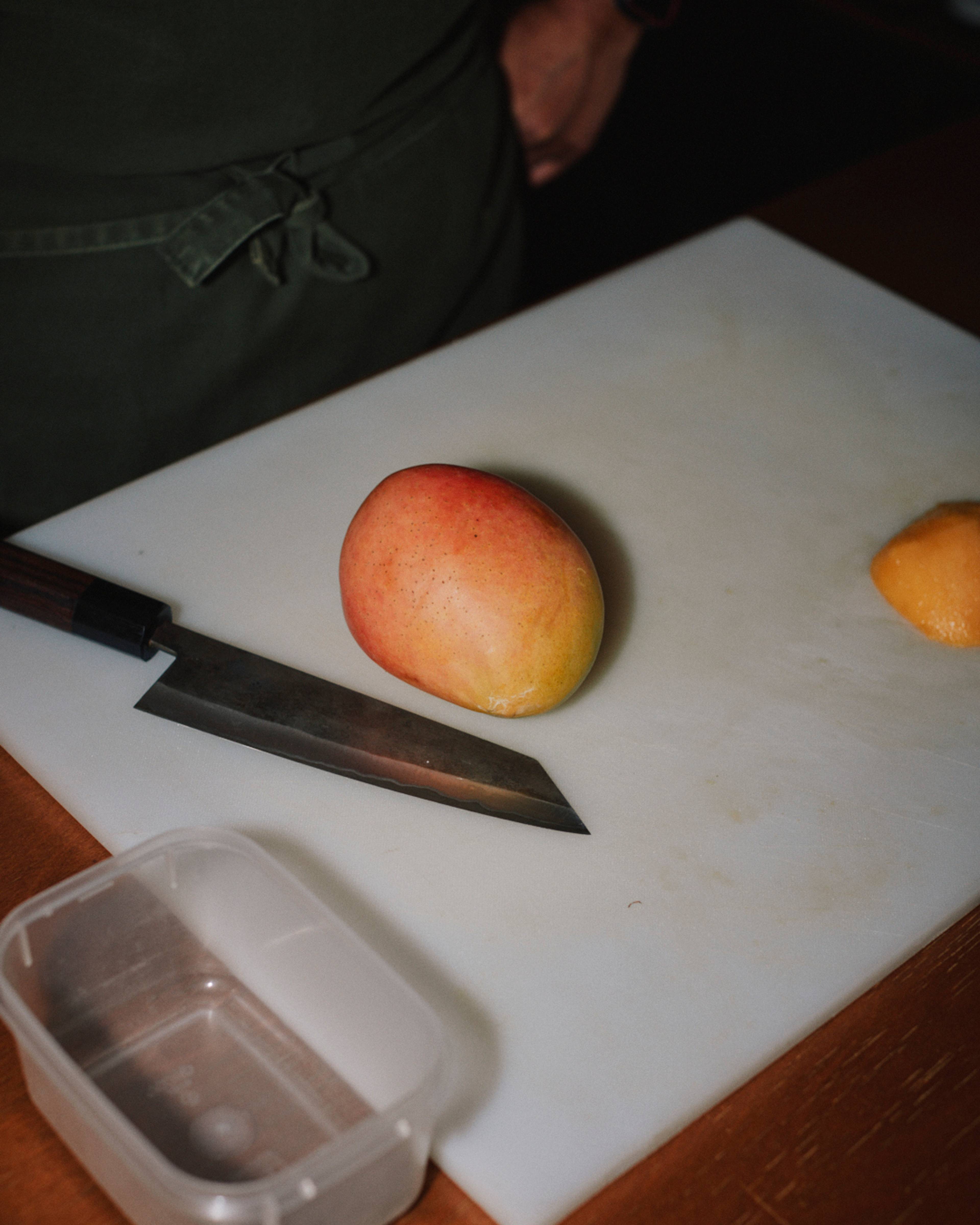 whole mango and knife on a chopping board