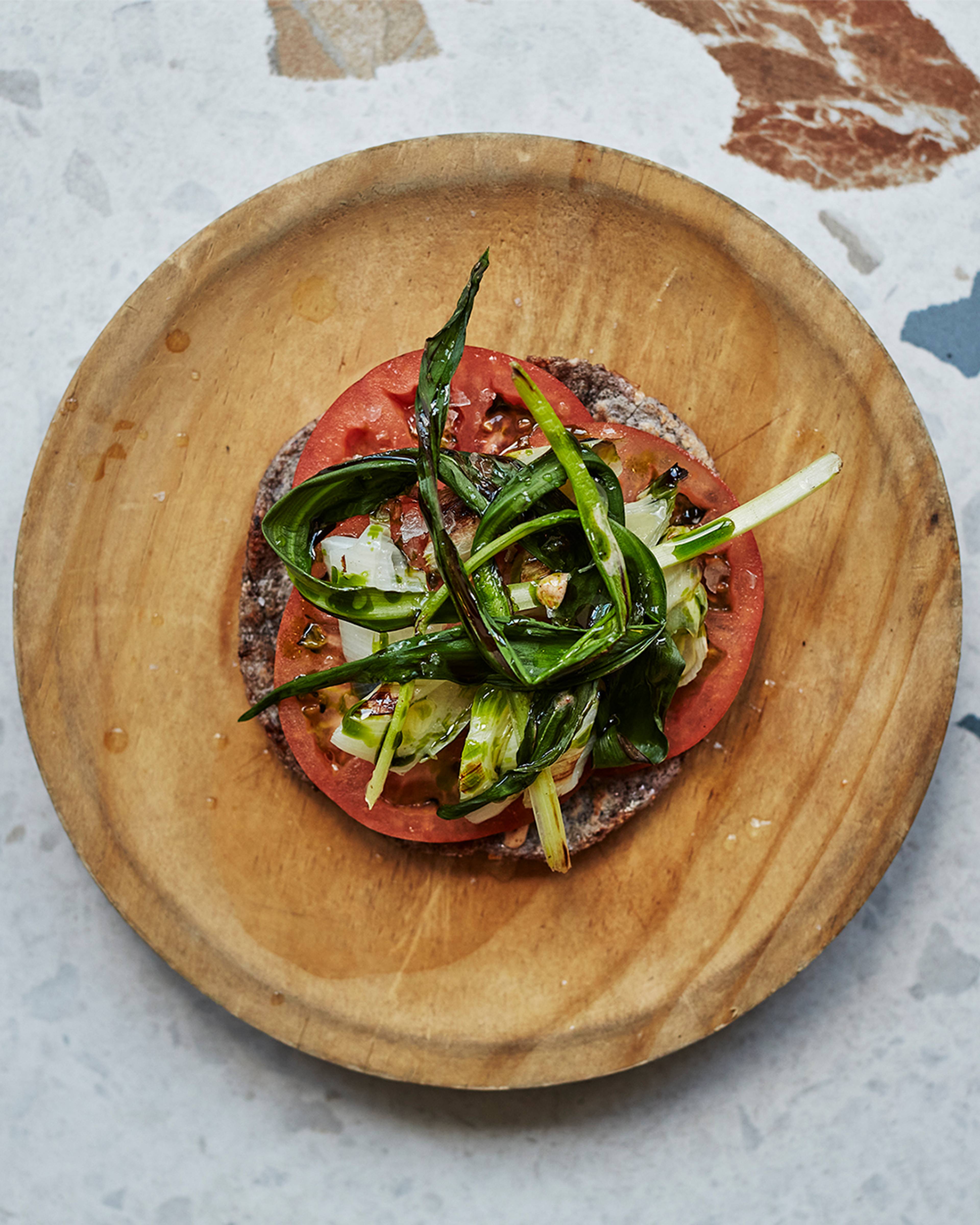 Tomato and calçot tostada overhead on a wooden plate