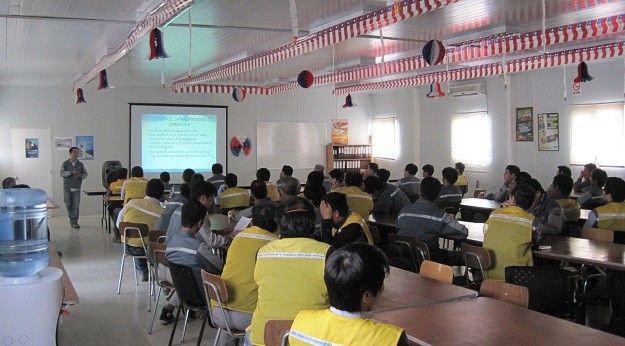 Instructor frente a trabajadores con chalecos de seguridad durante una capacitación en aula