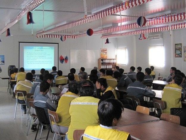 Instructor frente a trabajadores con chalecos de seguridad durante una capacitación en aula