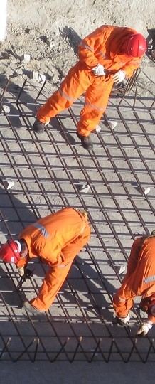 Operarios con ropa de trabajo naranja armando una malla de hierro