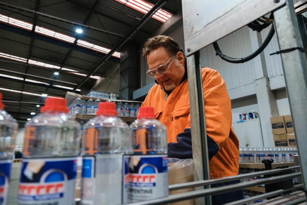 a man in an orange vest watches a machine paint a white line on the road