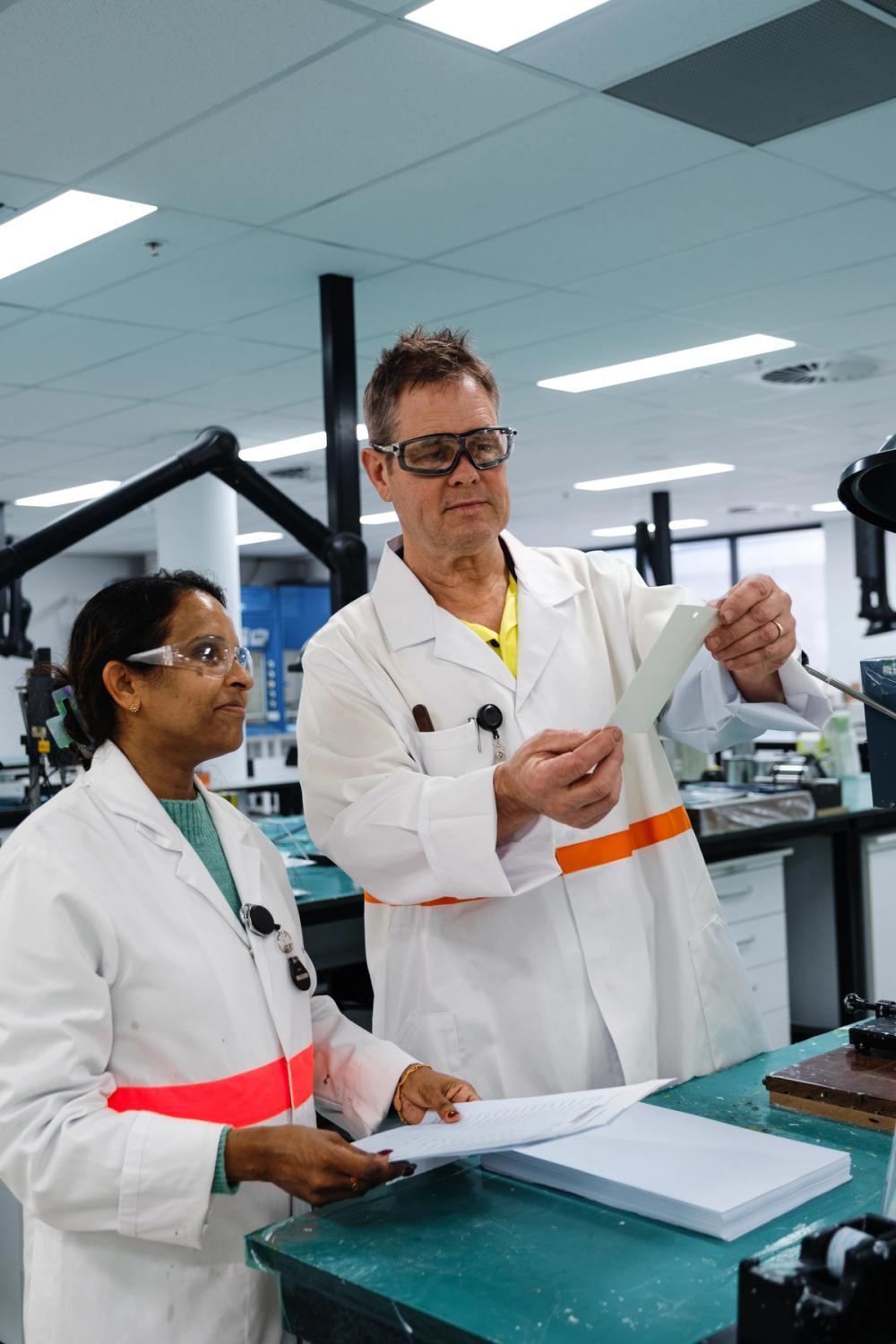 a man and a woman in lab coats are looking at a piece of paper a man and a woman in lab coats are looking at a piece of paper