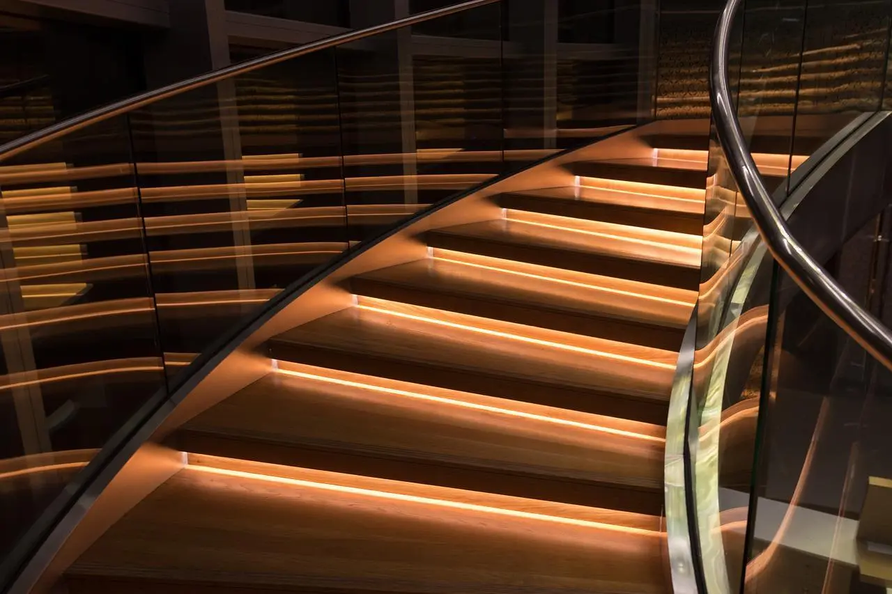 Curved staircase with glass railing, a steel handrail and LED-lit wooden steps