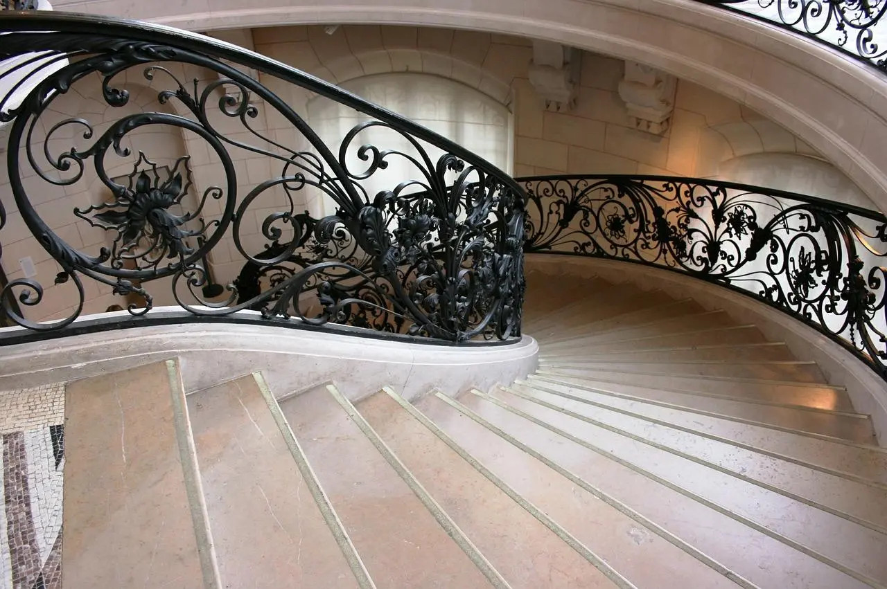 Curved marble staircase with an ornate black wrought iron floral railing