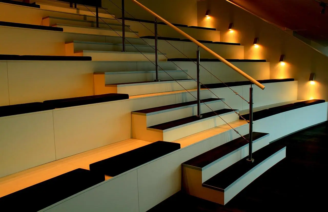 Wide lit steps with a thin steel cable railing and a wooden handrail