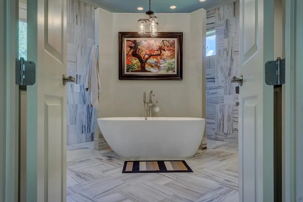 Freestanding white bathtub under a painting in a marble-tiled bathroom