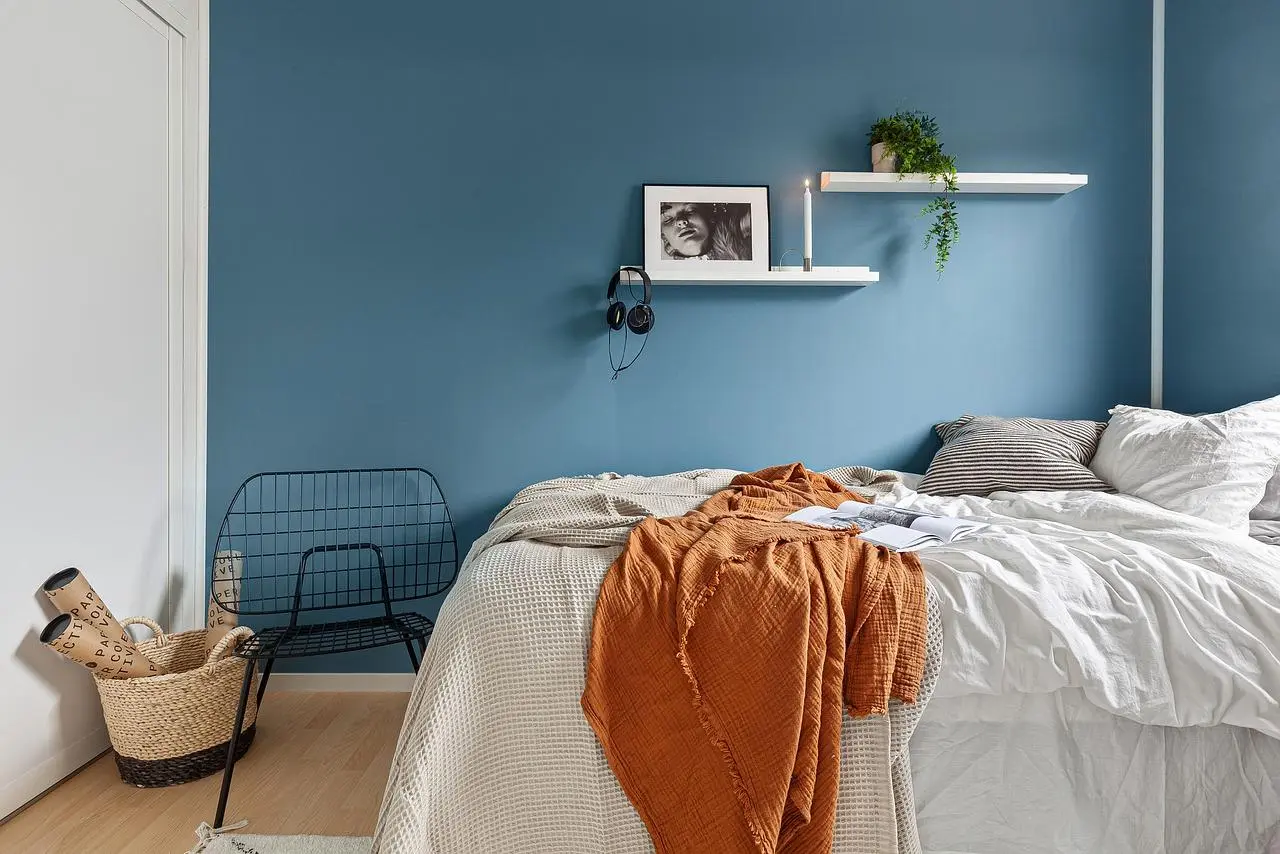 Bedroom with a calm blue wall, white bedding and an orange throw
