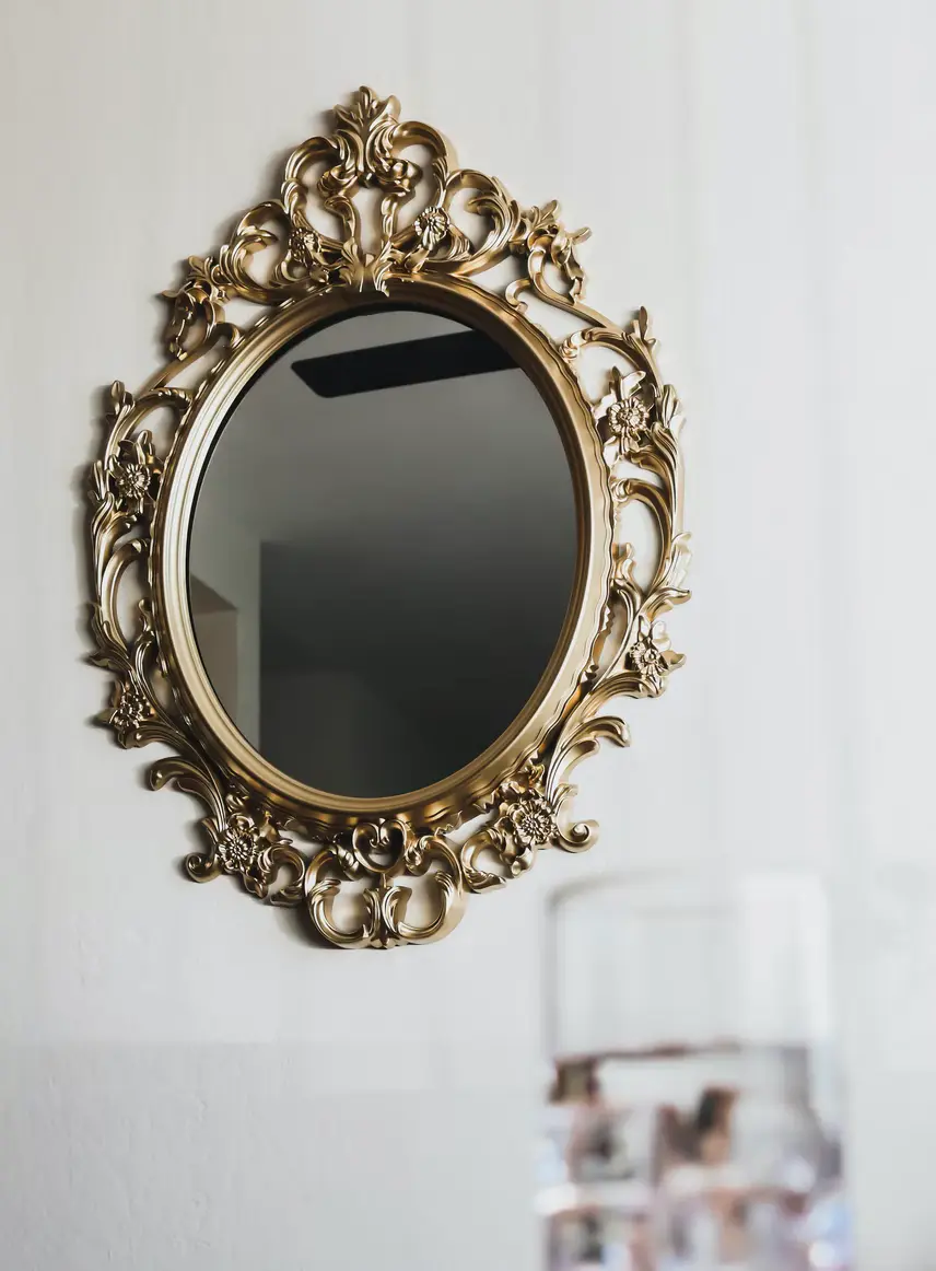 Oval mirror in an ornate gold baroque frame hanging on a white wall