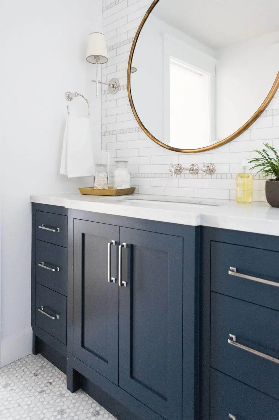 Navy blue bathroom vanity with a white countertop and a round brass mirror