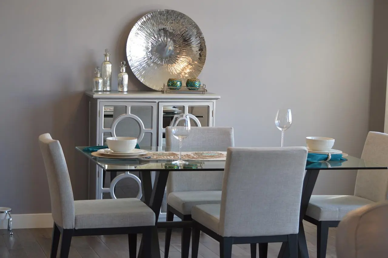 Glass dining table with grey upholstered chairs and a mirrored sideboard with a silver plate