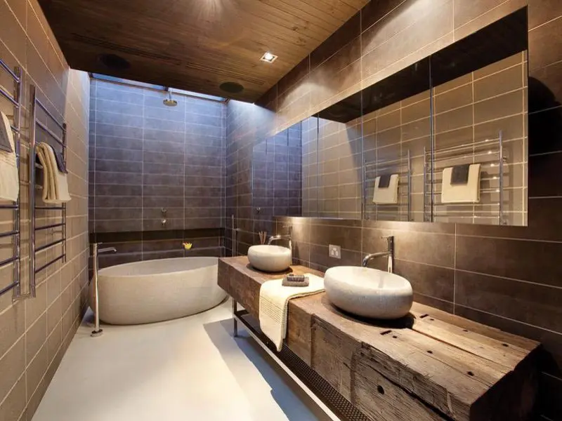 Dark tiled bathroom with a rustic wooden vanity, two vessel sinks and a freestanding tub