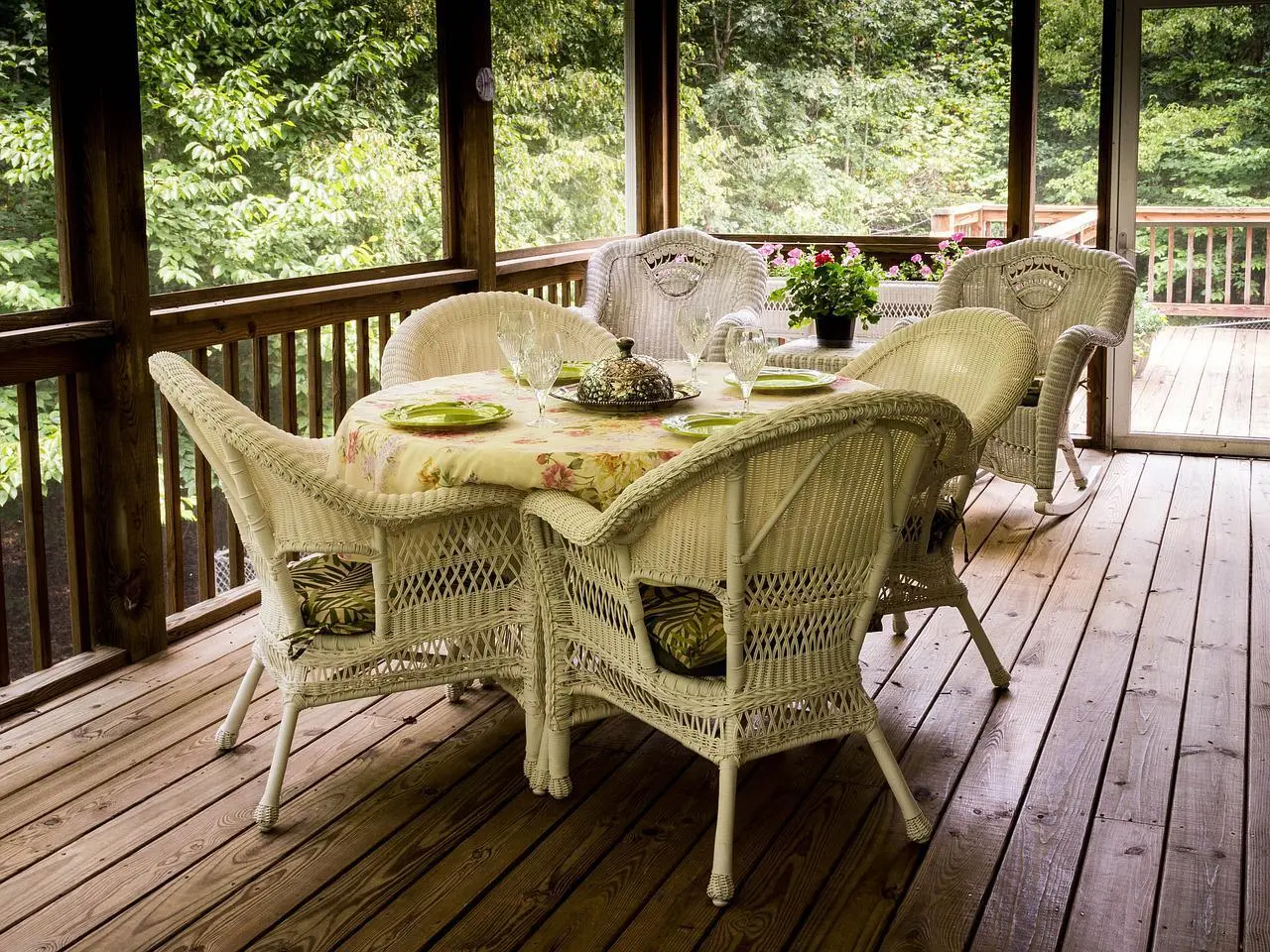 Covered wooden porch deck with a white wicker dining table and chairs