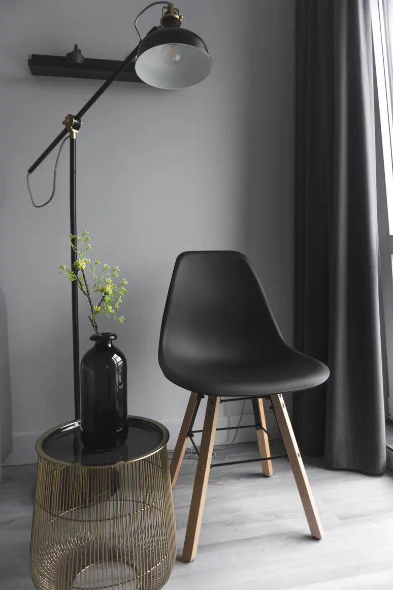 Grey corner with a black chair, a black floor lamp and a brass side table with a vase