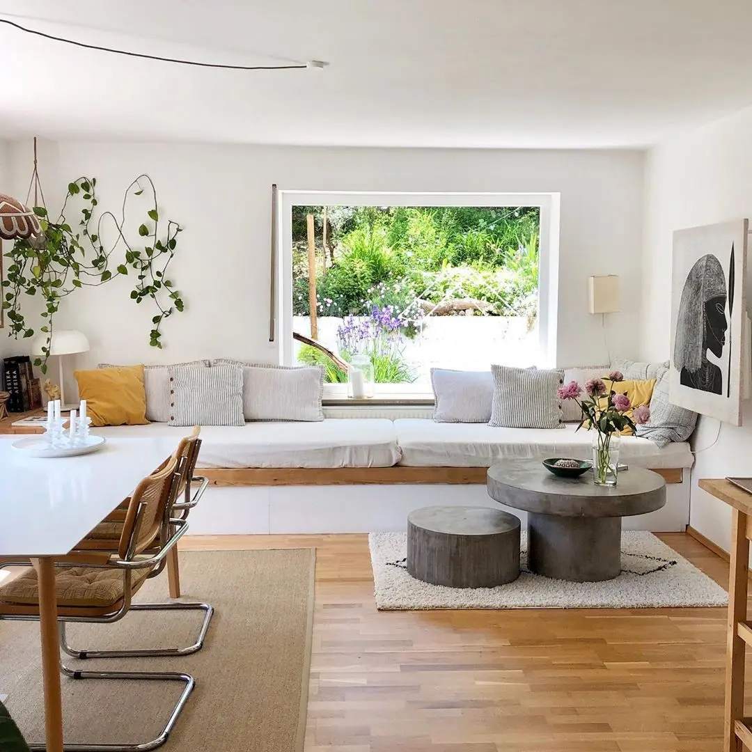 Bright living room with a built-in window seat, round coffee tables and hanging plants