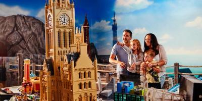 A family admires a Lego model of a cathedral with a clock tower.