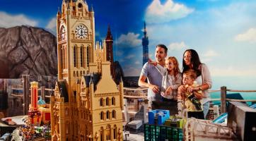 A family admires a Lego model of a cathedral with a clock tower.