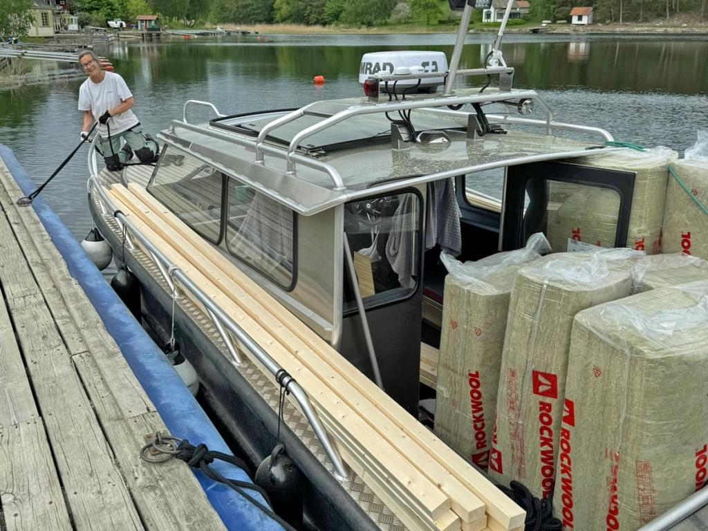 Flanör vid bryggan lastad med reglar och isolering, en person förtöjer på fördäck.