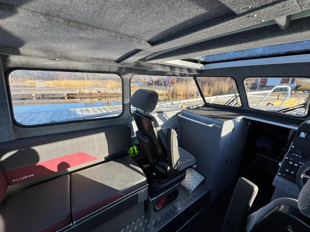 Hytten med förarstol och en sittbänk längs sidan, och utsikt genom de stora fönstren.