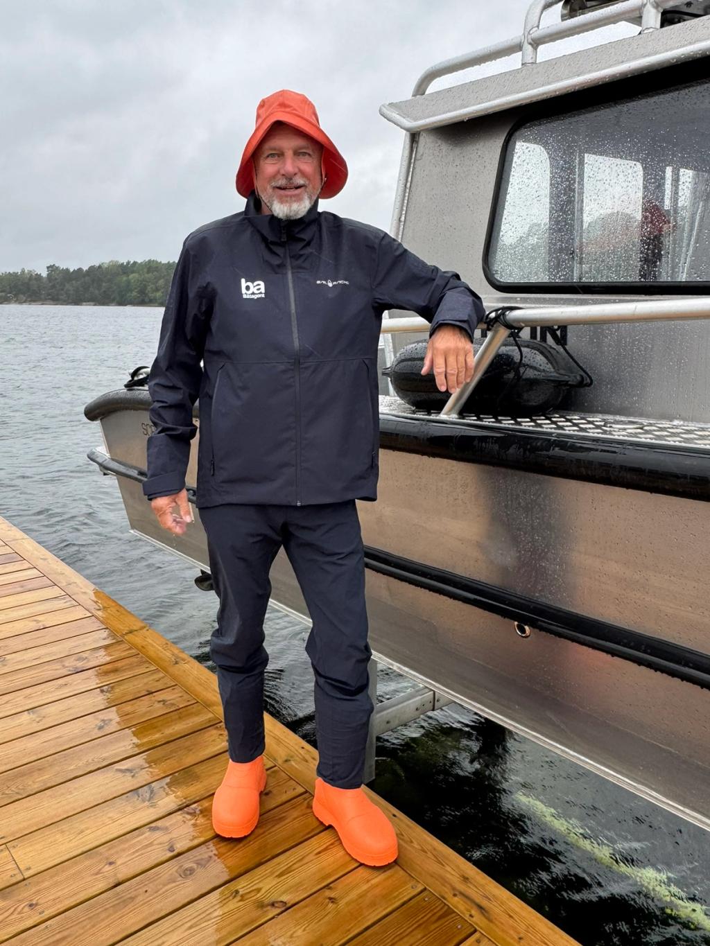 Niklas Forsén i orange sydväst och orange stövlar på bryggan, med handen på Flanörs reling.