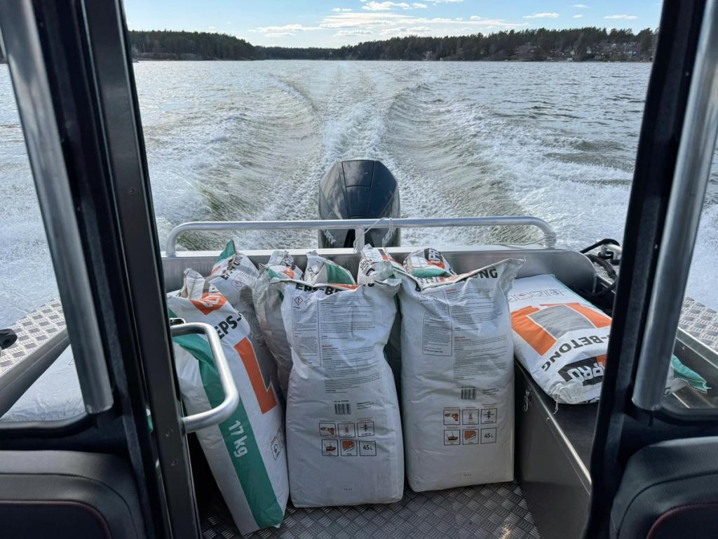 Säckar med betong och byggmaterial lastade i Flanörs akter under gång, med kölvattnet bakom.