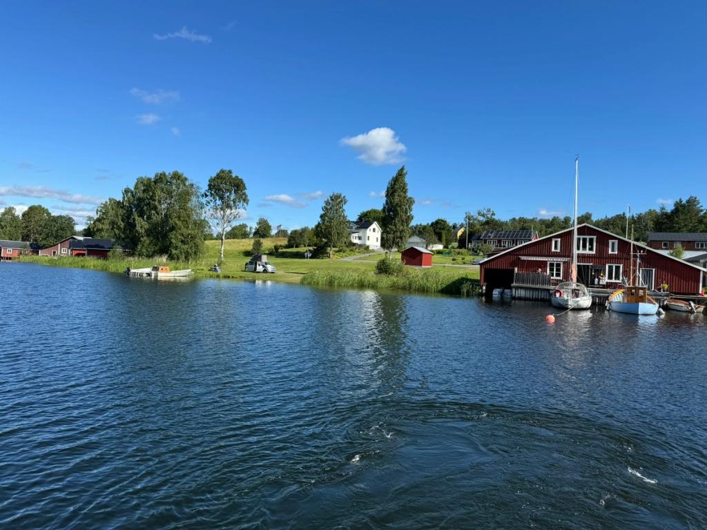 Skärgårdsvik med ett rött båthus och bryggor i sommarsol.