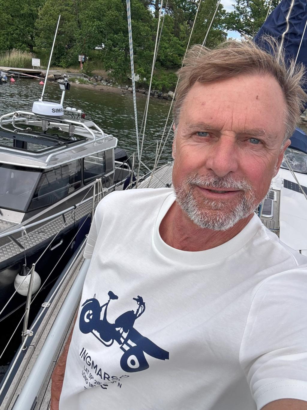 Niklas Forsén ombord i vit t-shirt, med en båt och skärgården bakom sig.