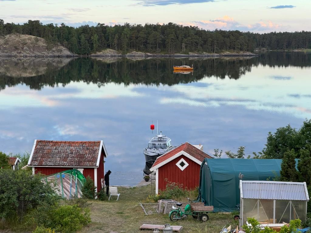 Spegelblankt vatten i kvällsljus, med röda sjöbodar och en båt förtöjd vid stranden.