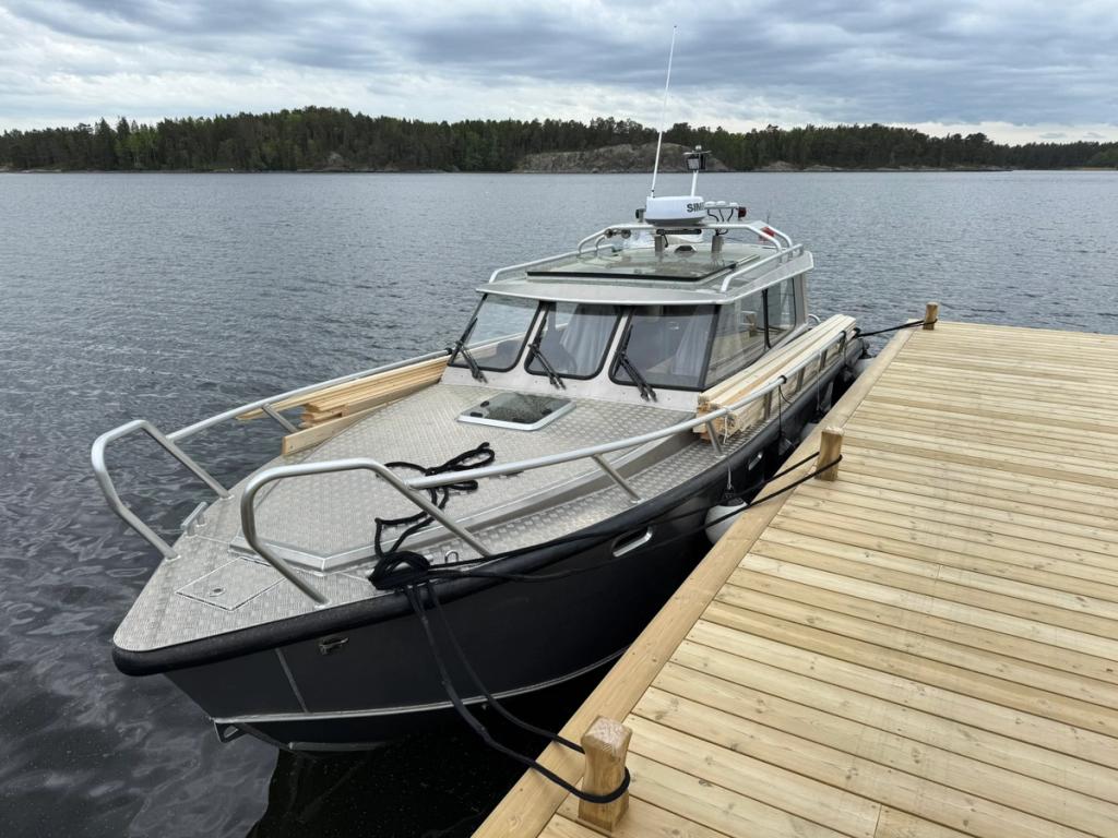 Flanör förtöjd vid en nybyggd brygga med virke lastat längs sidodäcket.