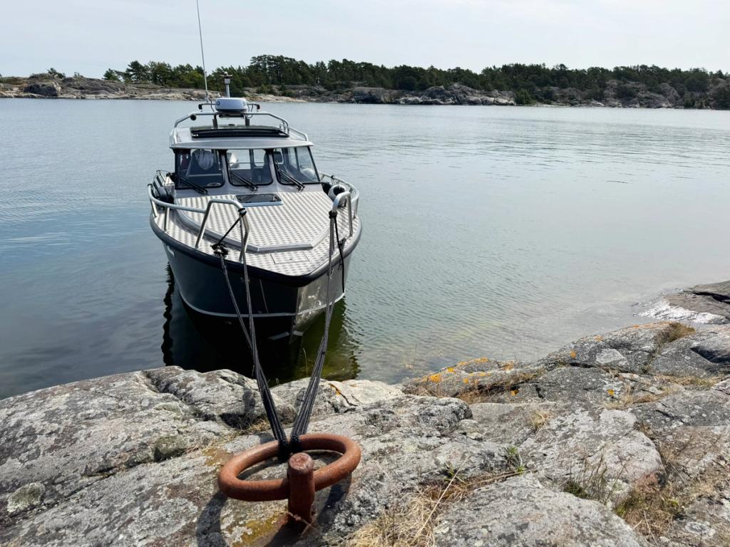 Flanör förtöjd med stäven mot berget, linor fästa i en järnring i klippan.