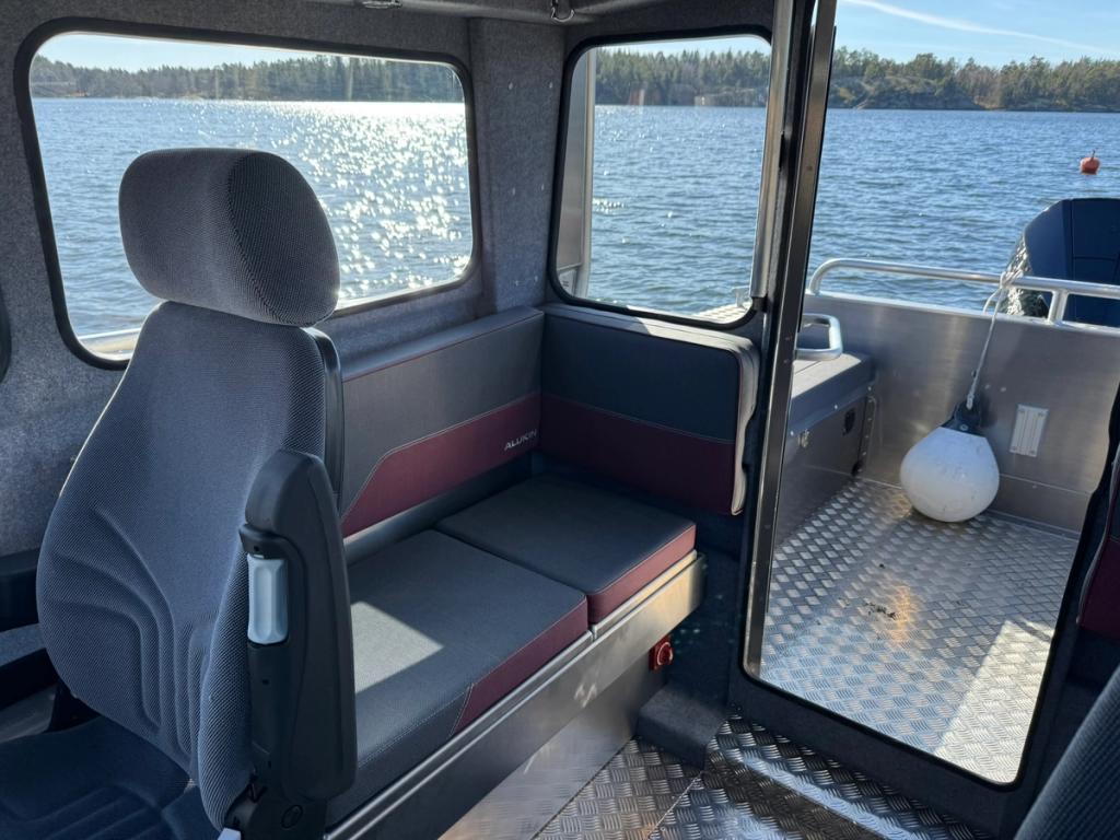 Förarstol och sittbänk i hytten, med solglittrande vatten utanför.