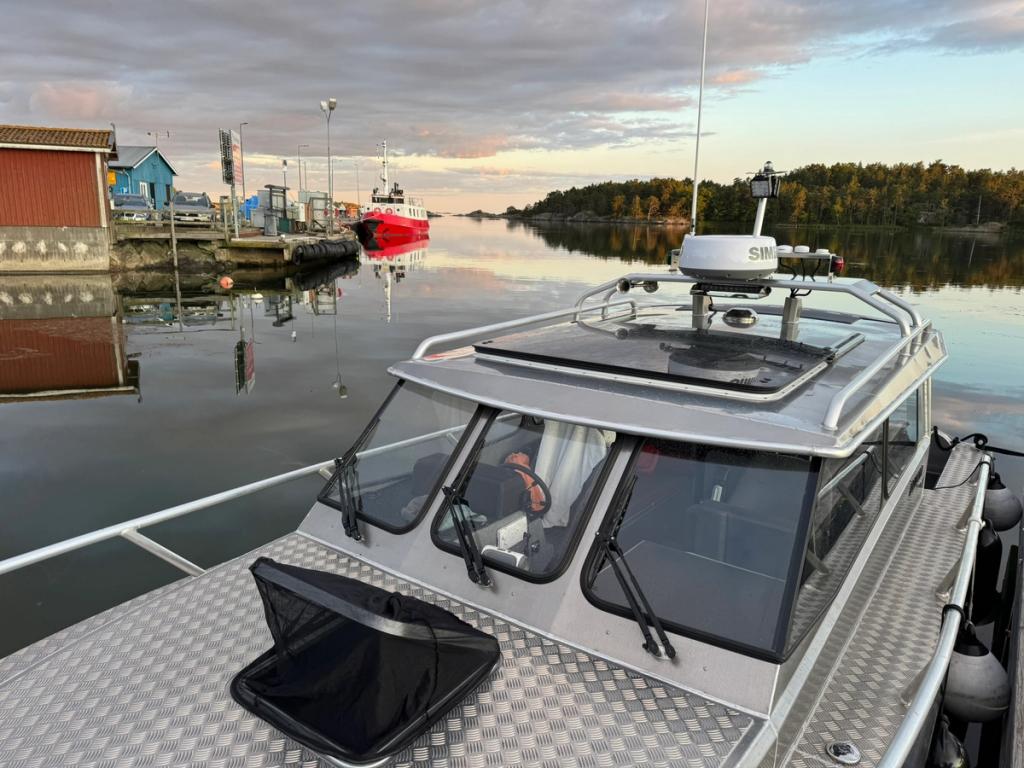 Flanörs fördäck vid kajen i gryningsljus, med en röd skärgårdsfärja längre fram.