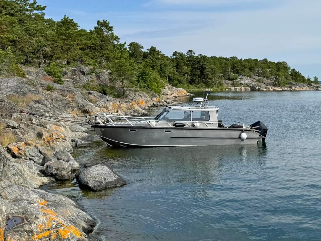 Flanör förtöjd mot klipporna i en naturhamn en sommardag.