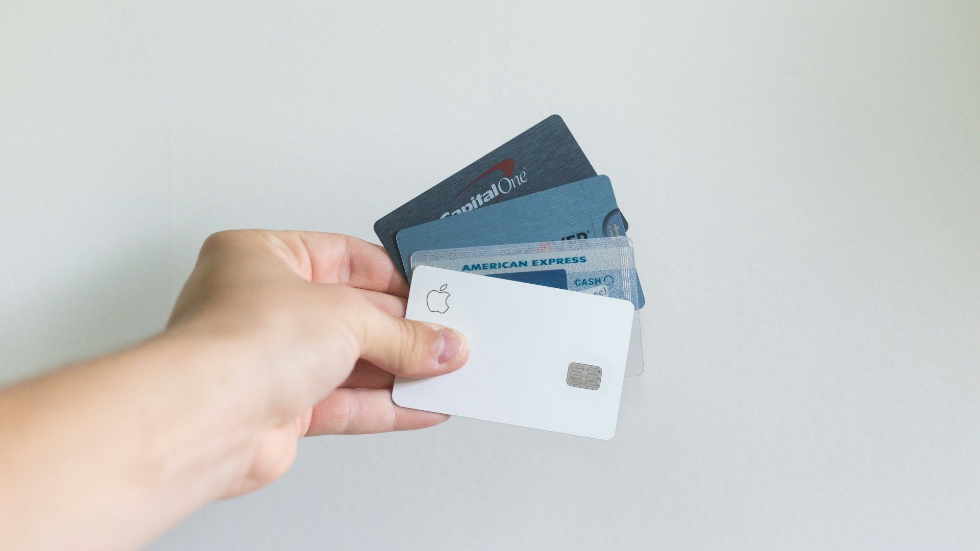 A person holding credit cards against a white background wall.