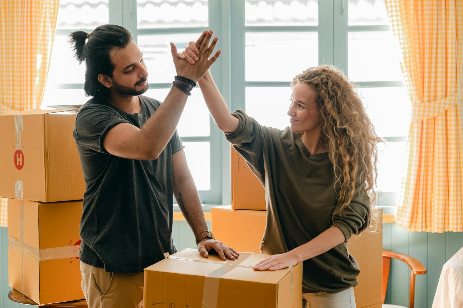 Couple giving high give standing near pile of boxes