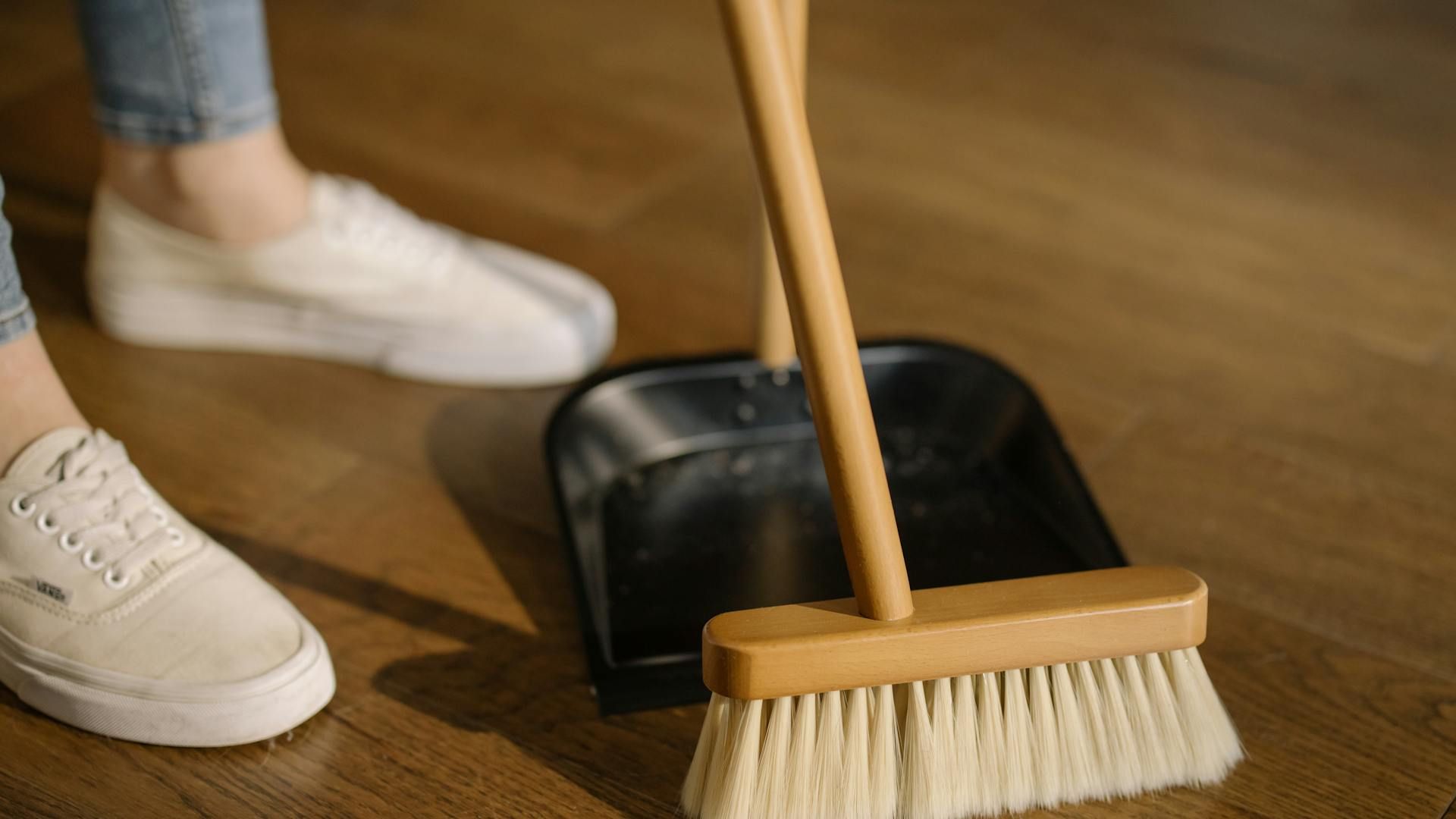 Person Wearing White Pants and White Socks Standing Beside Brown Broom