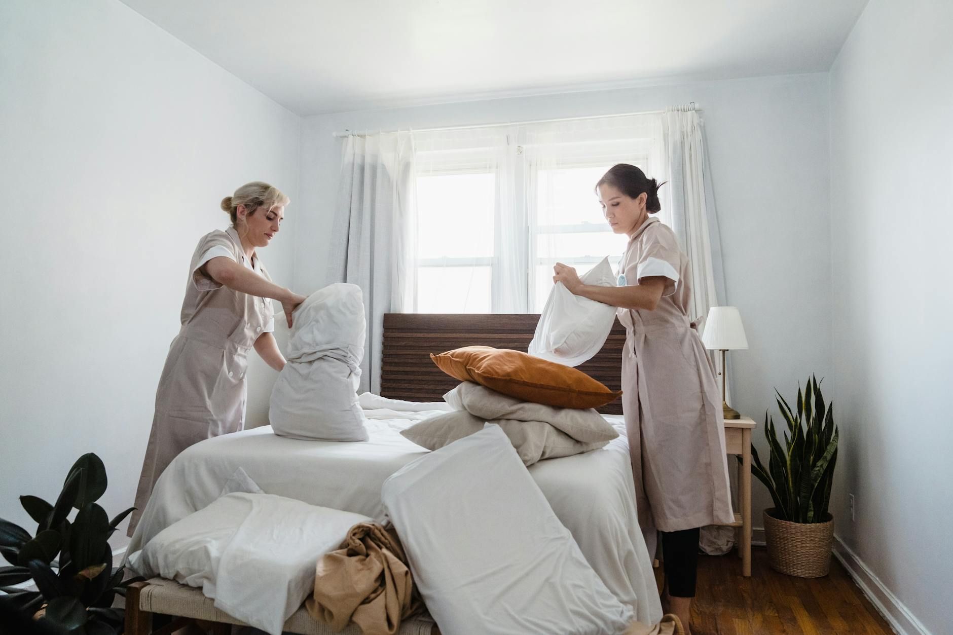 Two women in uniforms tidying a bed, creating a clean and welcoming space.