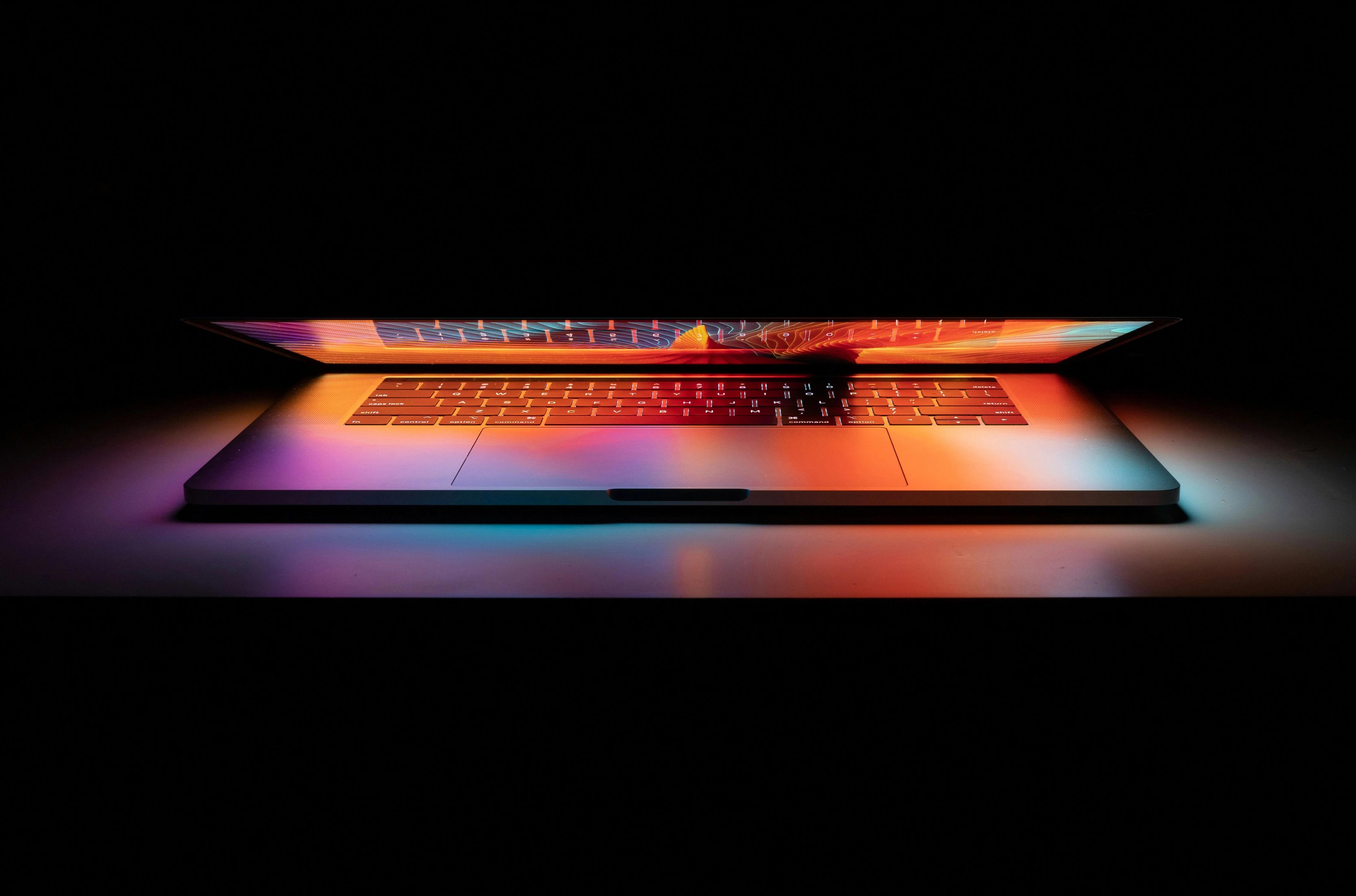 Blog_Technology_partially open laptop in a dark space reflecting a colorful screen on keyboard (Web Optimized)